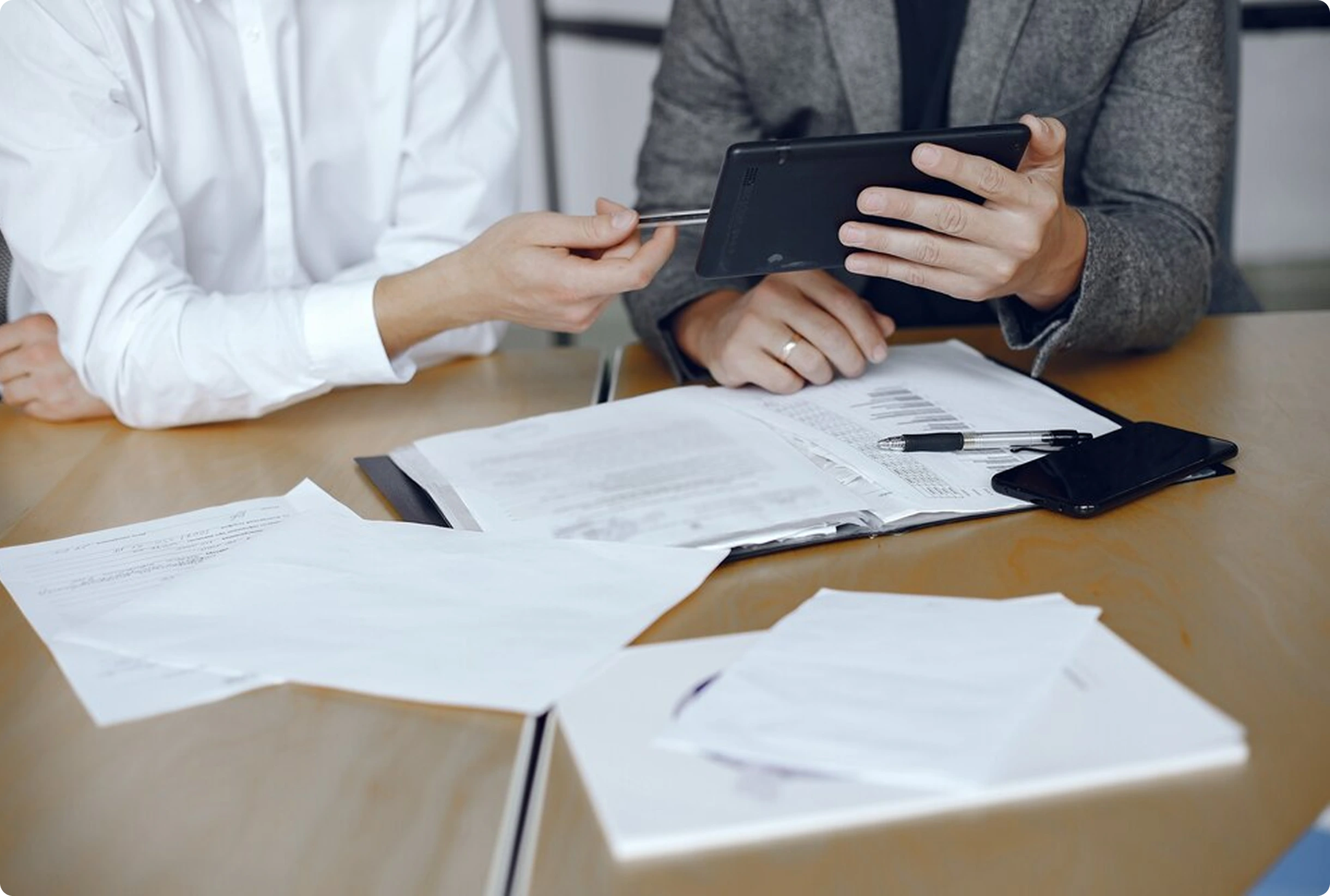 Two professionals reviewing documents and data on a tablet at a desk