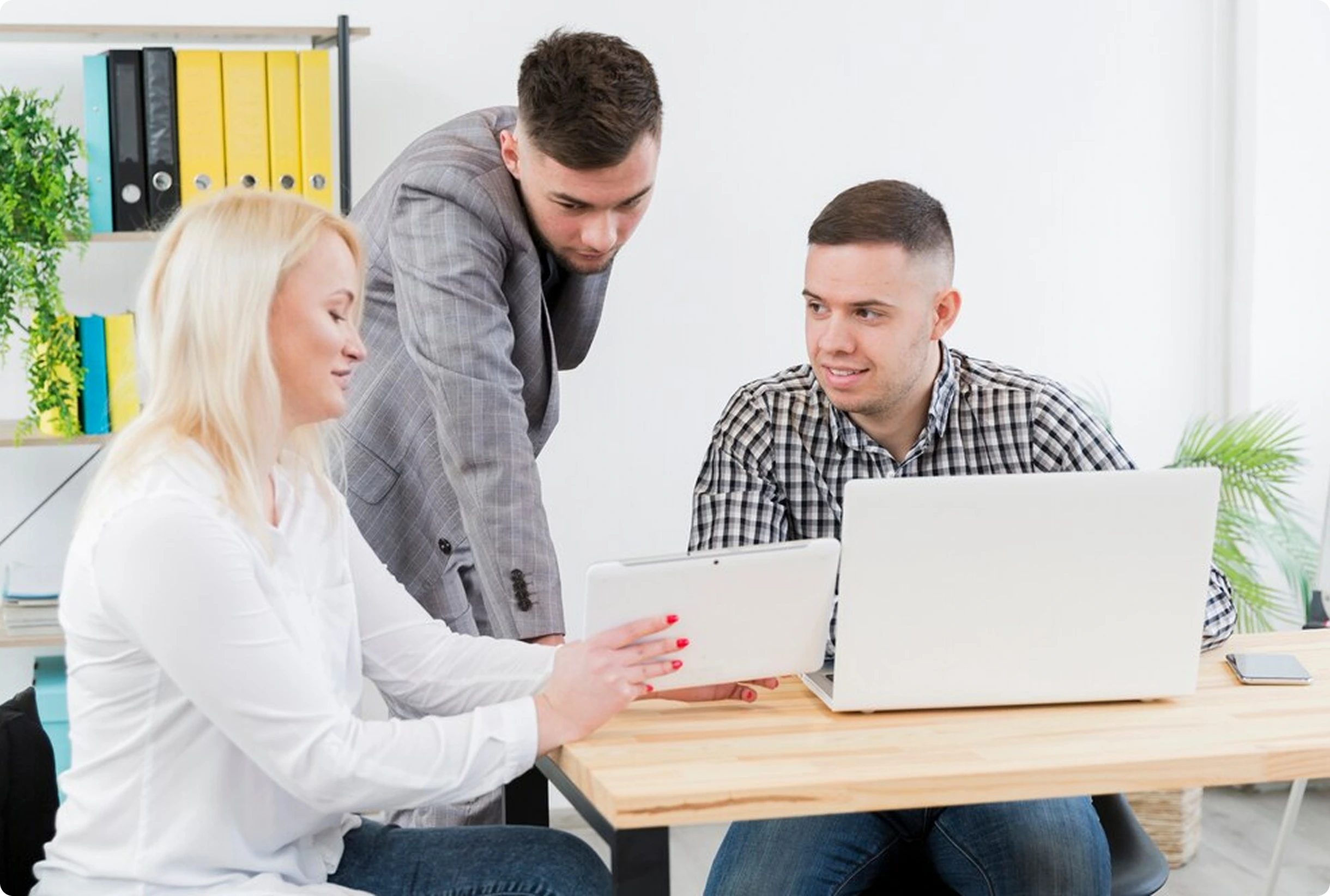 Three colleagues collaborating in a bright, modern office using laptops and a tablet